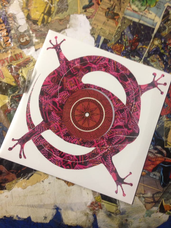 Cover of 'Feels Like' 10" - a coiled pink, orange & brown lizard with its head at the centre, its one visible eye with contrasting patterns forming the centre label of the 10" record
